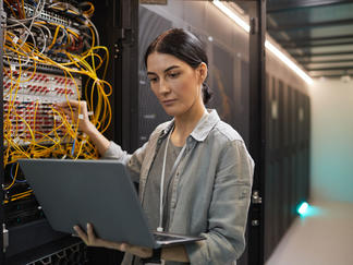 Technician checking a network with her laptop in the server room.
